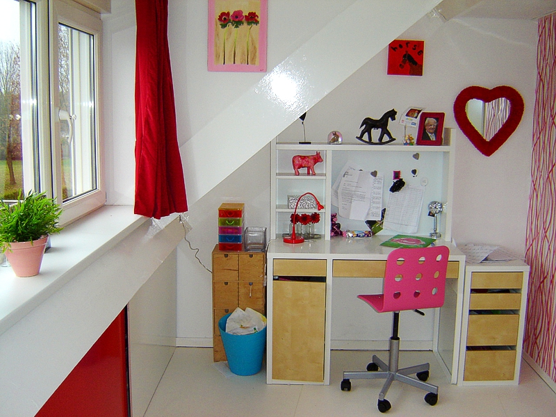 Bureau en rode inbouwkasten onder het schuine dak