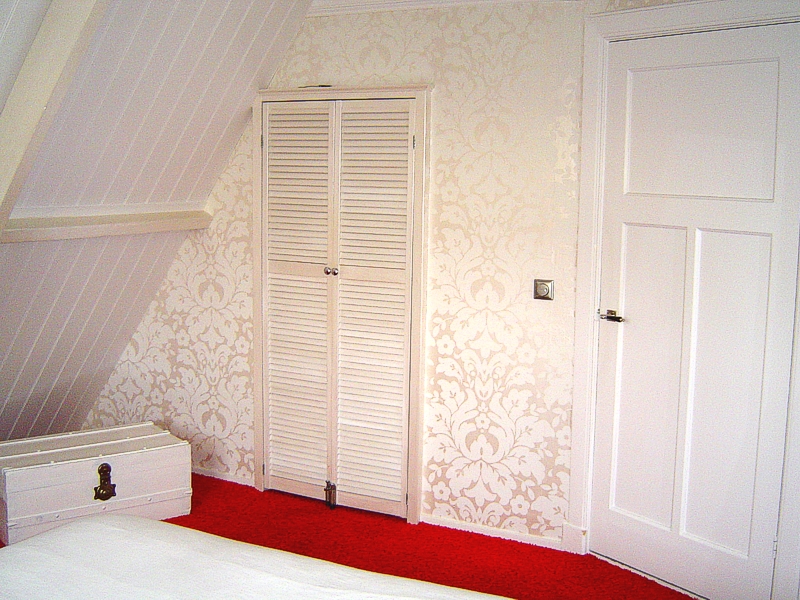 Afgewerkte zolder met louvredeur, behang en rood tapijt